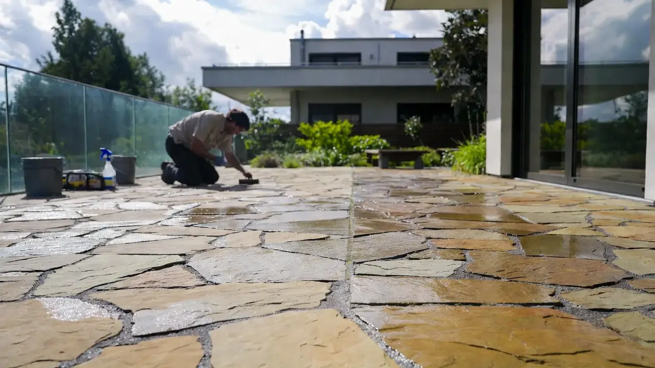 Techniker trägt Oberflächenversiegelung auf Natursteinterrasse nach Reinigung auf – zeigt versiegelte und unversiegelte Bereiche, professionelle Bodenpflege in Zürich, Schweiz.